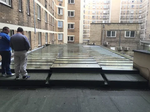 Broad flat roof between brick apartment buildings, with two people standing at the left