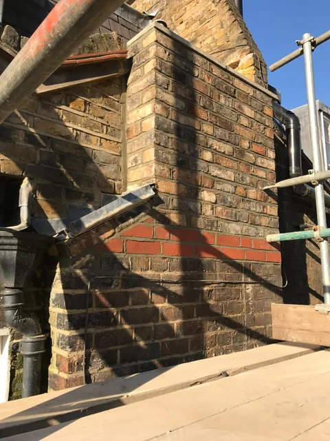 Brick chimney with scaffolding and repair materials around its base.