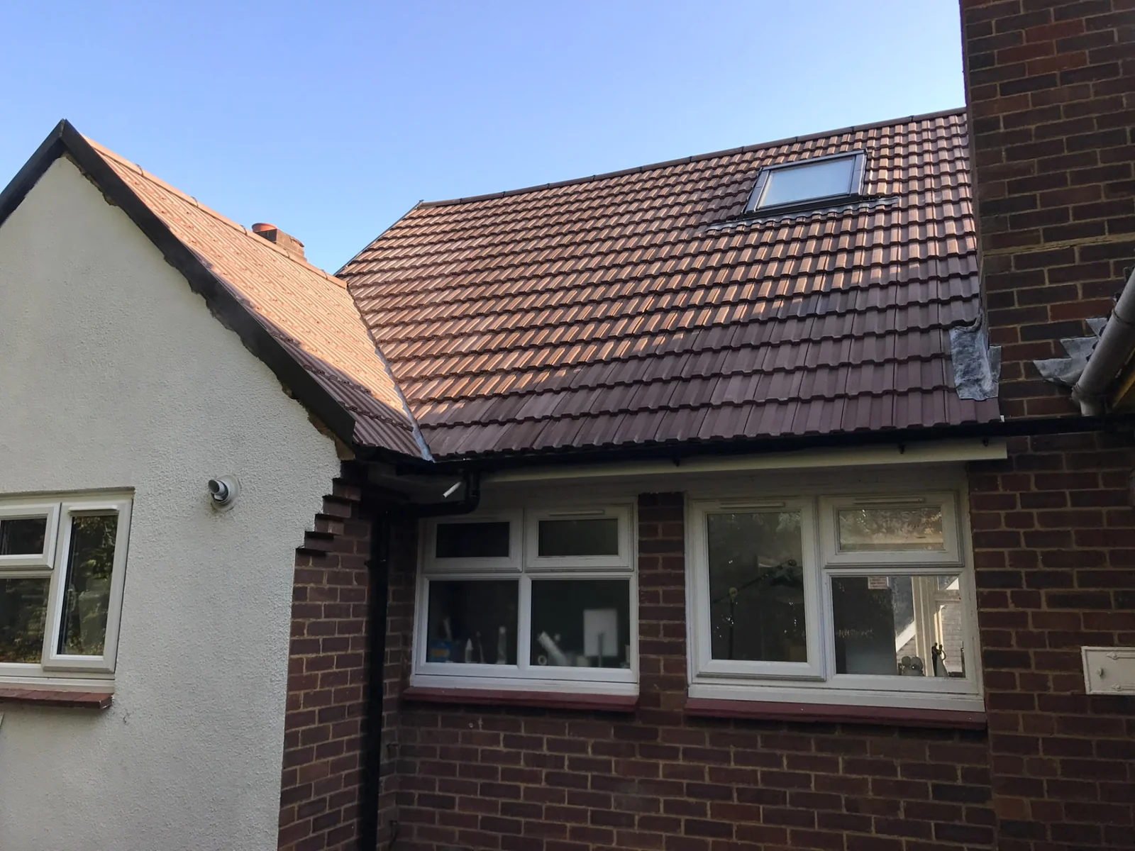 Completed brown tiled pitched roof with a rooflight above a brick house.