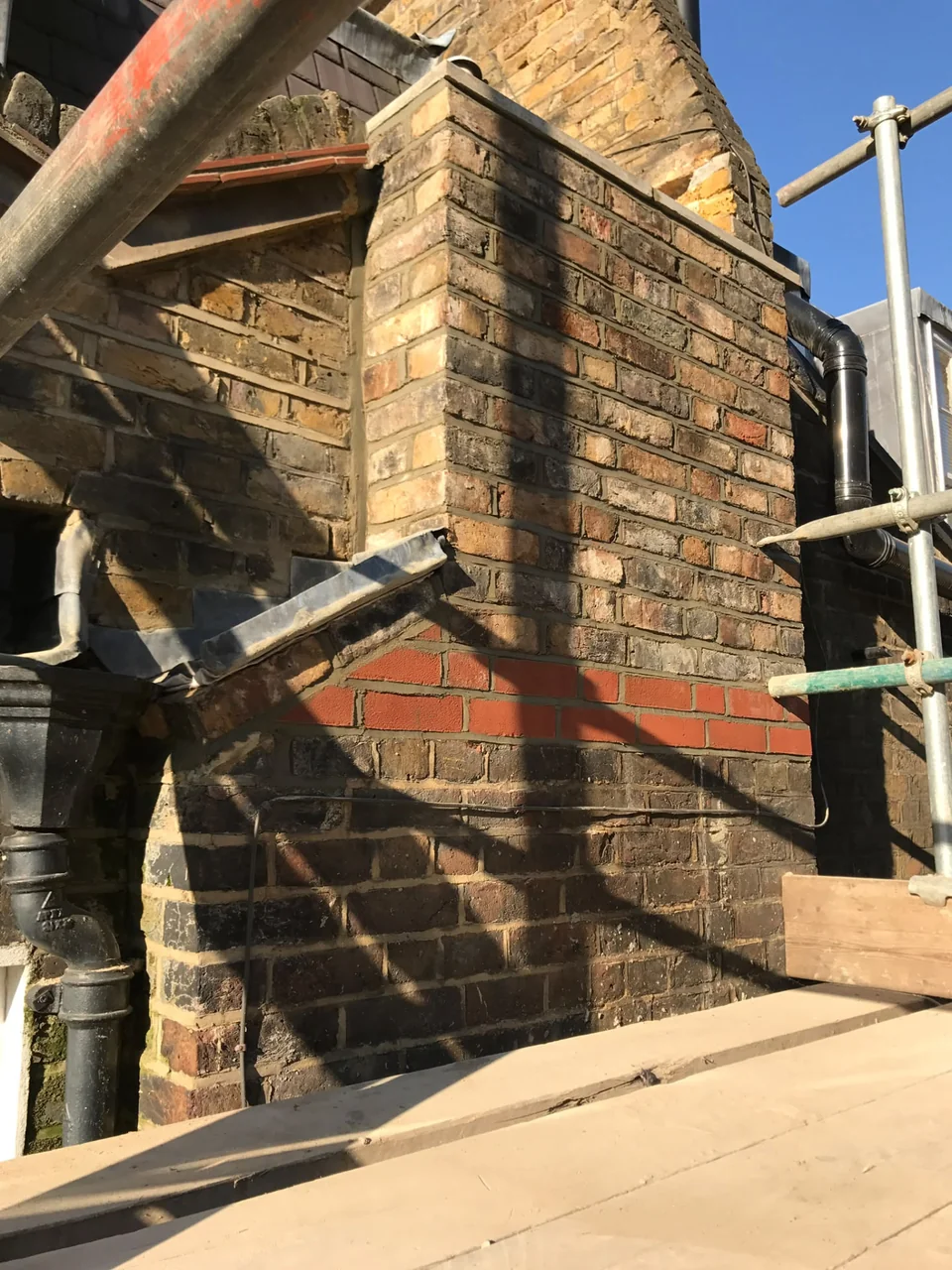 Brick chimney with scaffolding and repair materials around its base.