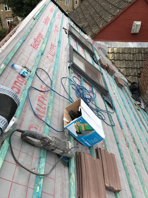 Roof under construction with exposed membrane, timber battens and bundled materials.