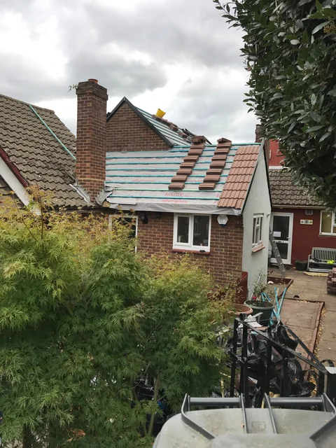 Pitched roof with exposed membrane and replacement tiles beside a chimney.