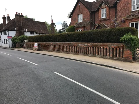 Brick boundary wall and hedge along a roadside, viewed from across the street.