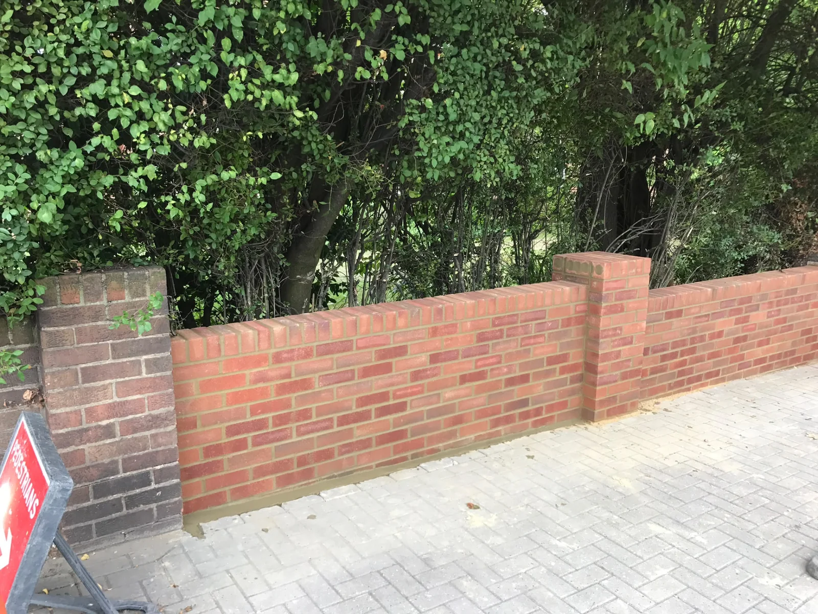 Red-brick boundary wall between brick piers beside a pavement