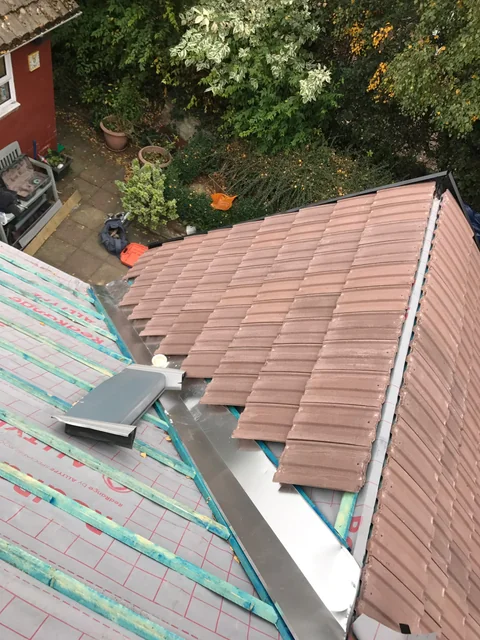 Pitched tiled roof viewed from above, with a strip of exposed roofing layer near the ridge.