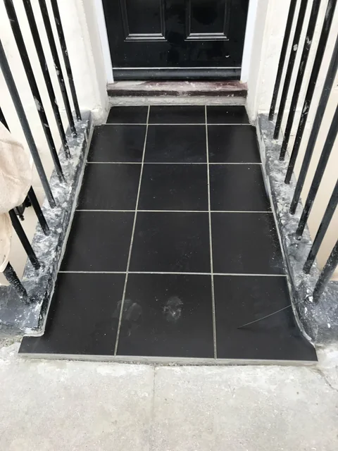 Completed dark tiled entrance landing between white walls and metal railings.