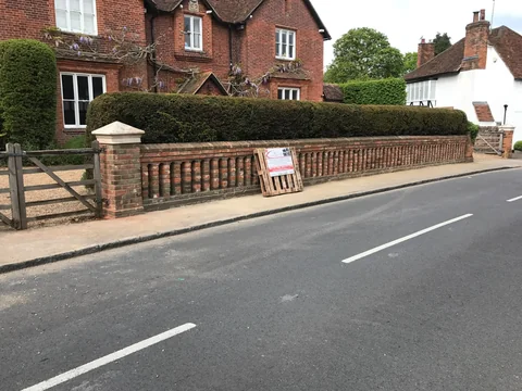 After: Brick boundary wall with pale coping and clipped hedge beside a road.