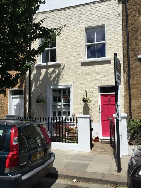 After: White multi-storey building frontage with a red entrance door and parked car.