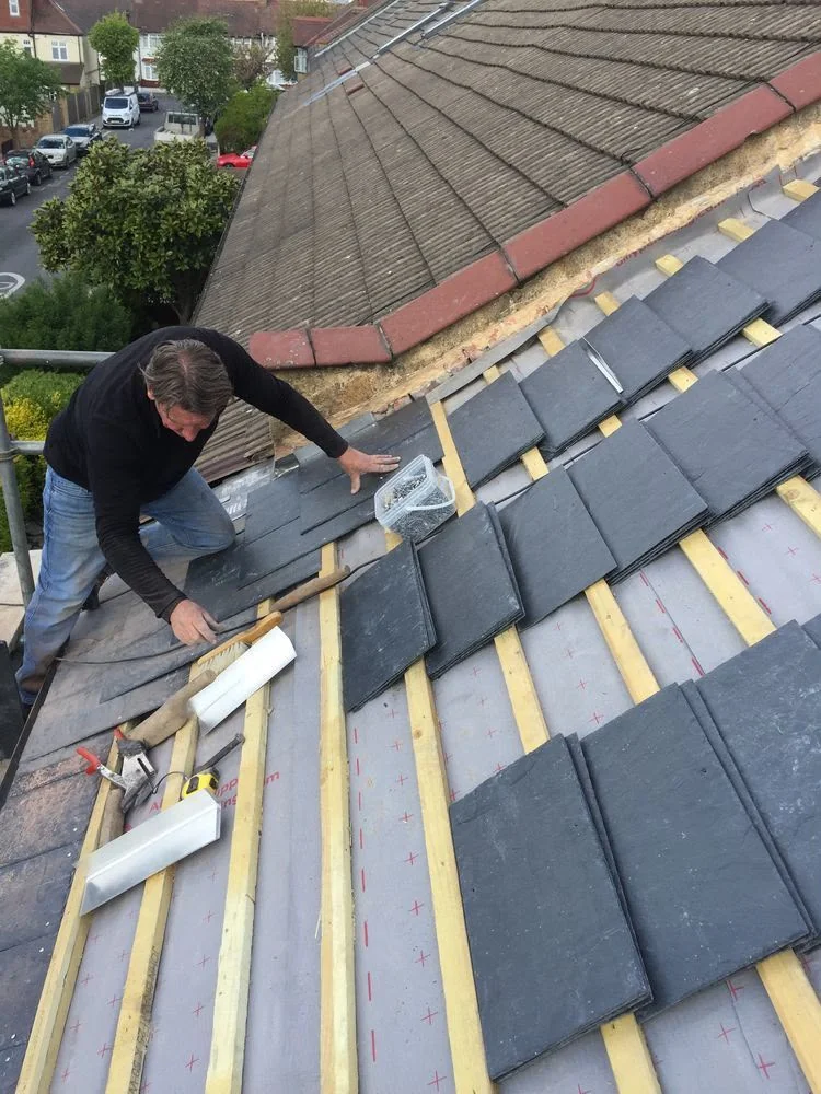 Worker laying dark roof slates over timber battens and roofing membrane